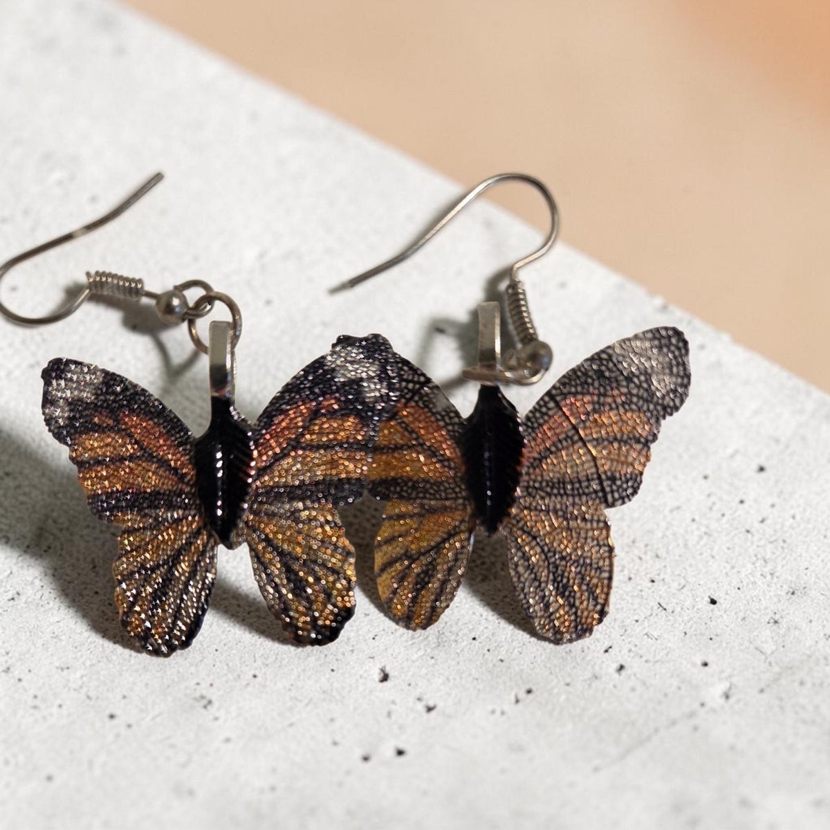 Blanca Closet brown butterfly earrings with intricate wing textures resting on a textured grey surface.