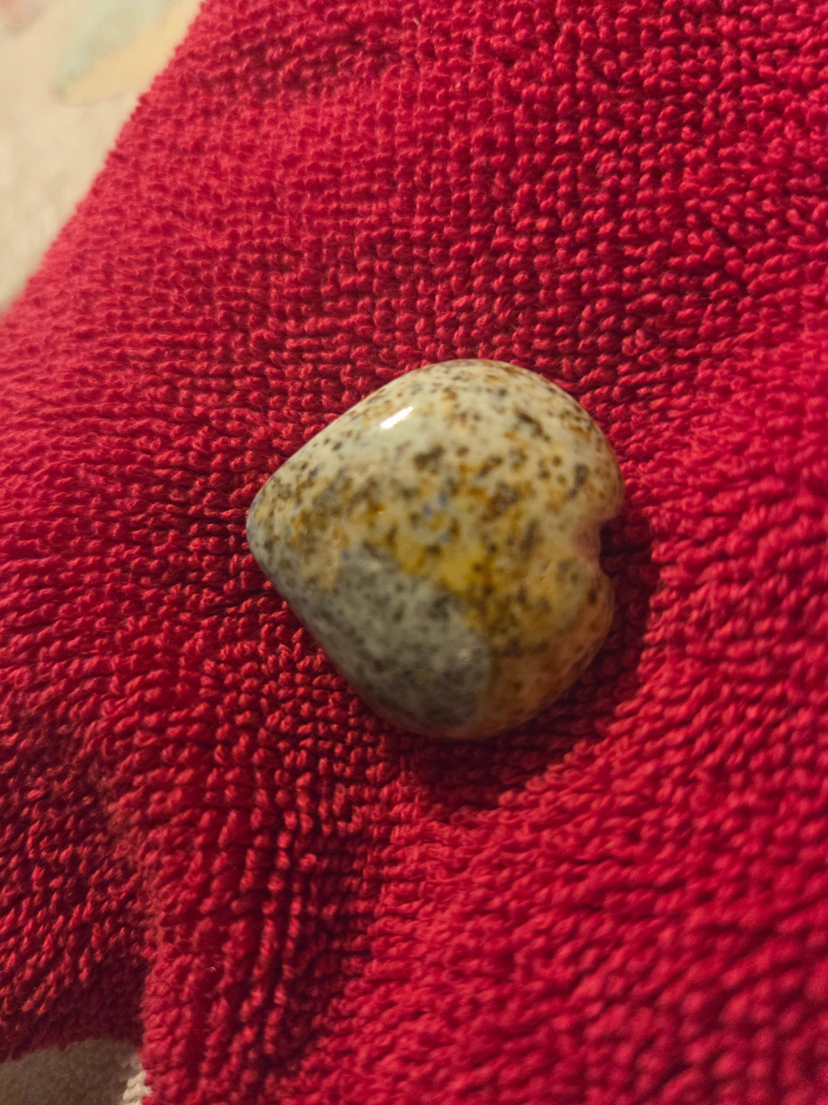 Blanca Closet polished stone heart ornament with speckled earthy tones and blue accents on a red textured fabric