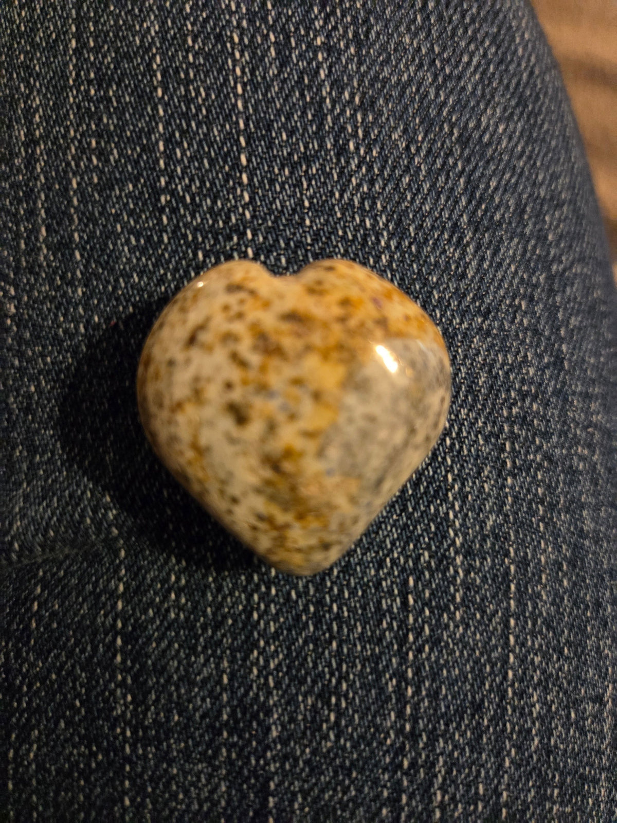Blanca Closet polished stone heart ornament with speckled tan and blue patterns resting on blue denim fabric.
