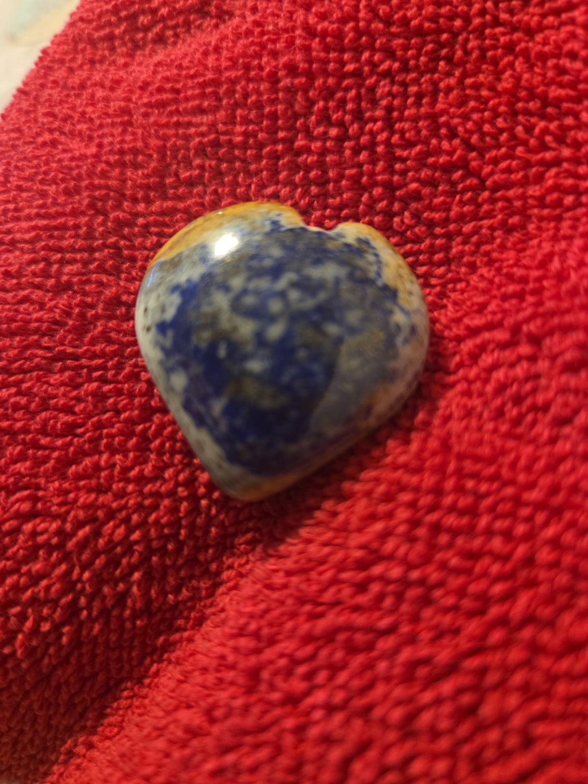 Blanca Closet polished stone heart ornament with blue, tan, and white patterns on a textured red fabric background.