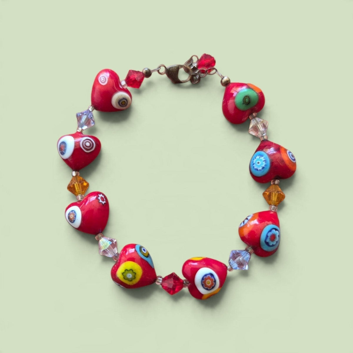 Blanca Closet red heart-shaped millefiori bead bracelet with crystal spacers on a light green background.